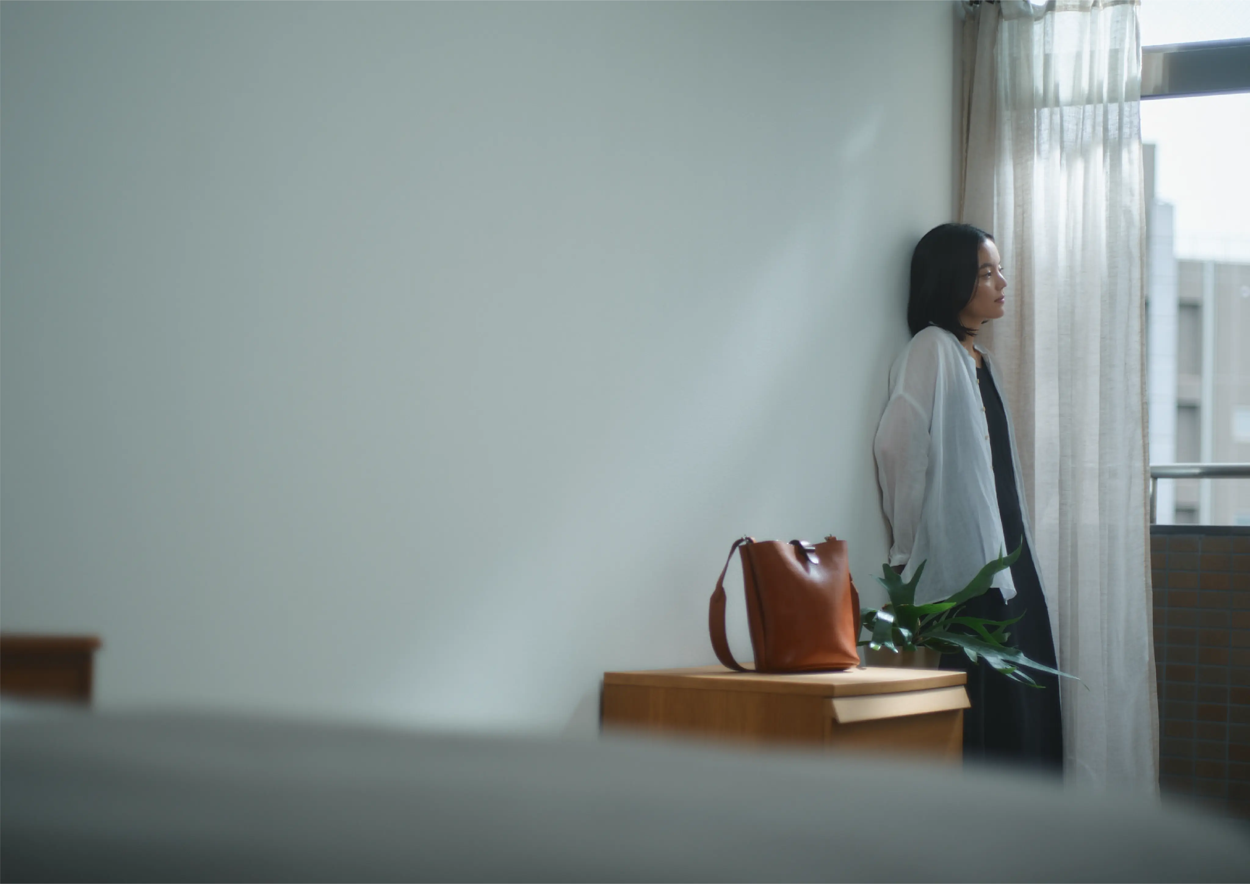 窓辺に立つ女性と革のバッグ